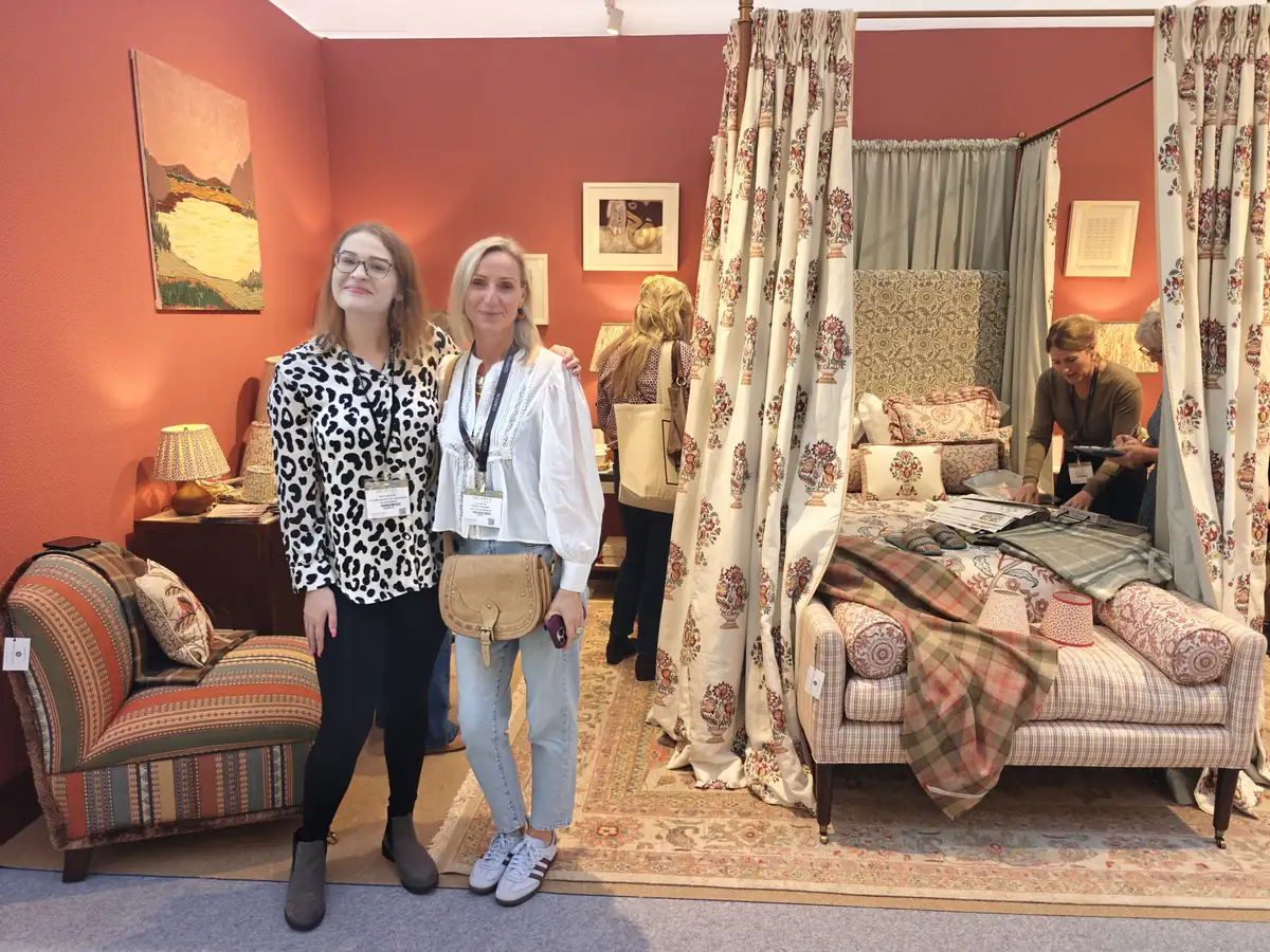 Lucy Kelvie on the Ian Sanderson stand at Decorex 2026, with a four-poster bed dressed in printed floral linen and checked fabrics