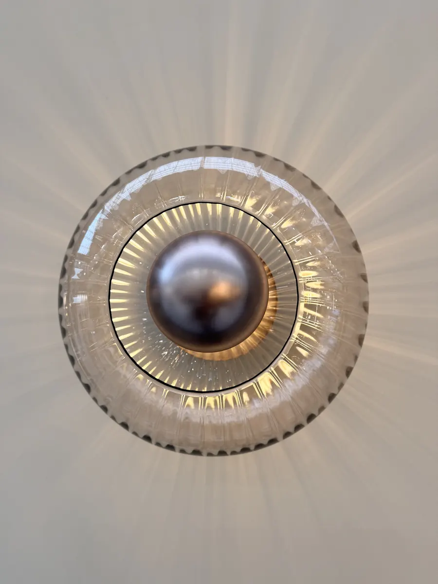 Industville round fluted glass wall light with a metal dome centre casting rays of light across a white wall at Decorex 2026