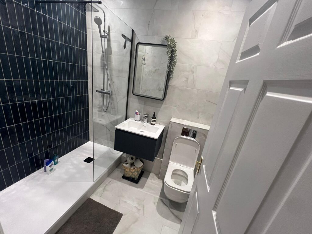 After: rental bathroom in Packington, Islington, redesigned by Lucy Kelvie with walk-in shower, glossy navy tiles, wall-hung vanity and marble-effect porcelain
