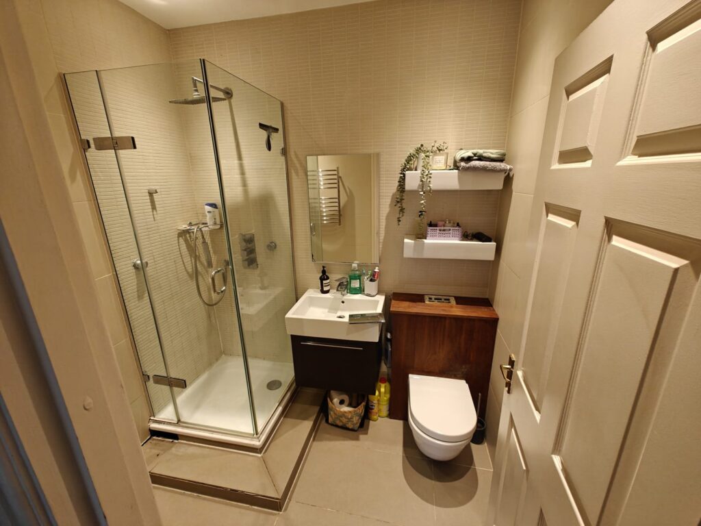 Before: dated beige-tiled bathroom with corner shower cubicle and boxed-in cistern in a rental flat in Packington, Islington