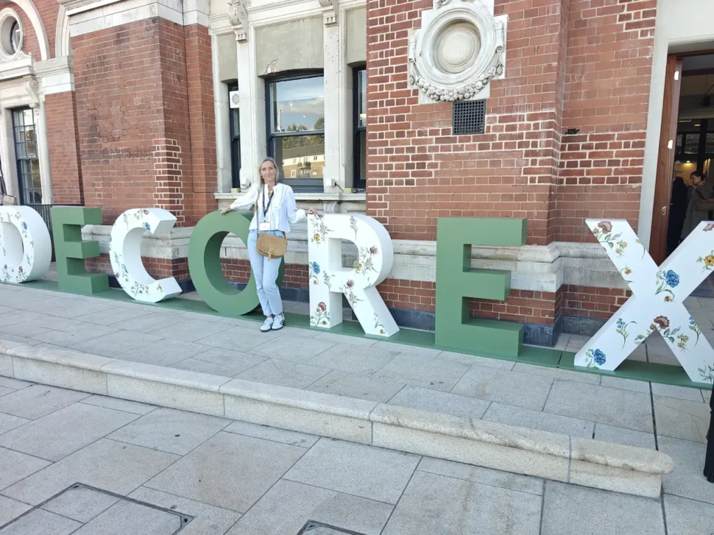 Interior designer Lucy Kelvie standing among the giant DECOREX letters outside Olympia London at Decorex 2026