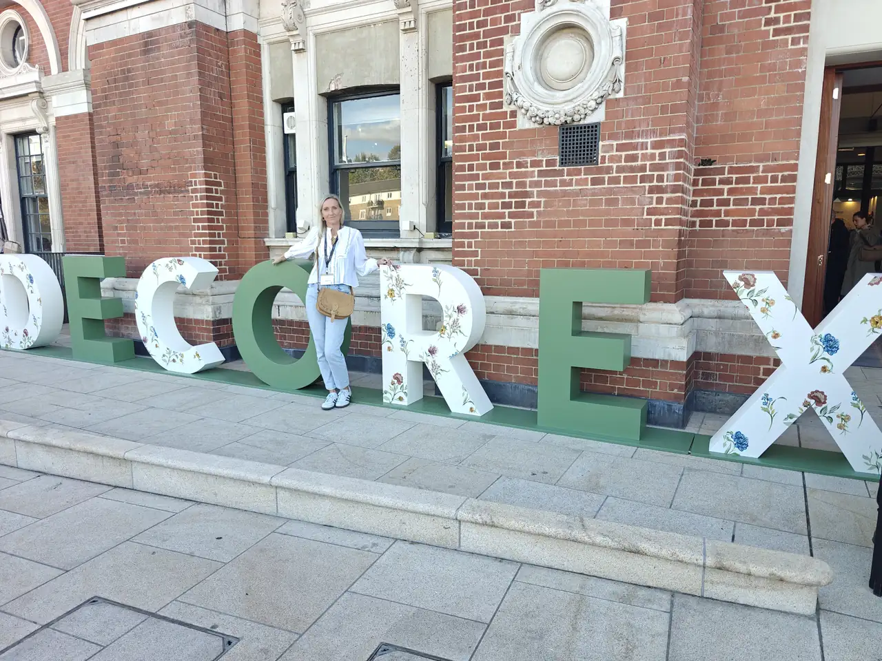 Interior designer Lucy Kelvie standing among the giant DECOREX letters outside Olympia London at Decorex 2026