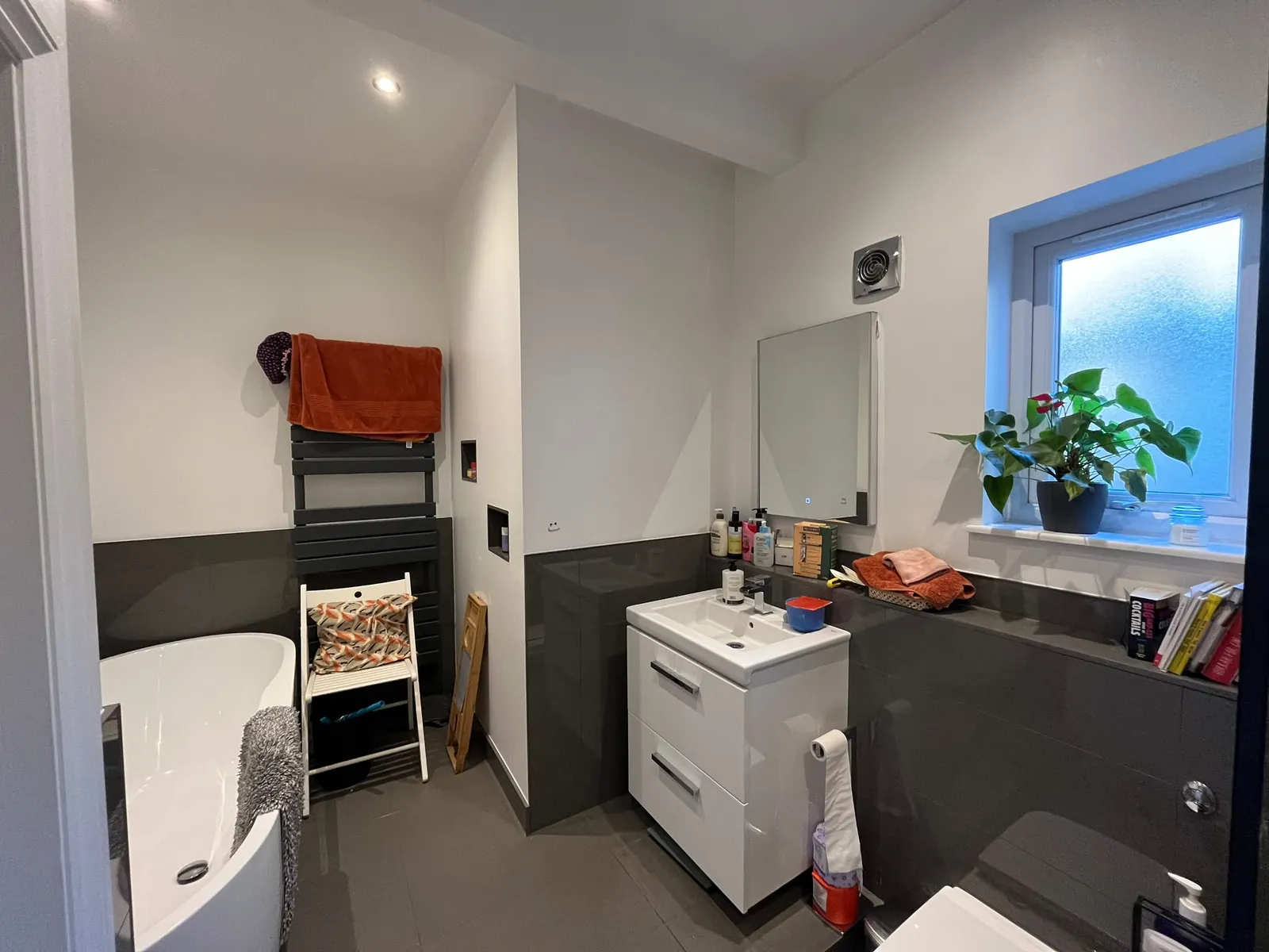 Main bathroom before the redesign, with white walls, dark grey tiles, a freestanding bath, a white vanity unit and a frosted window