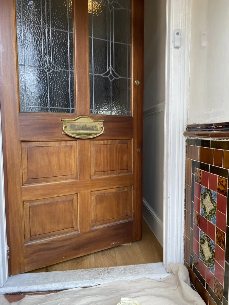 Inner front door before painting, in stripped wood with leaded glass panels and a tarnished brass letterbox, beside original patterned wall tiles