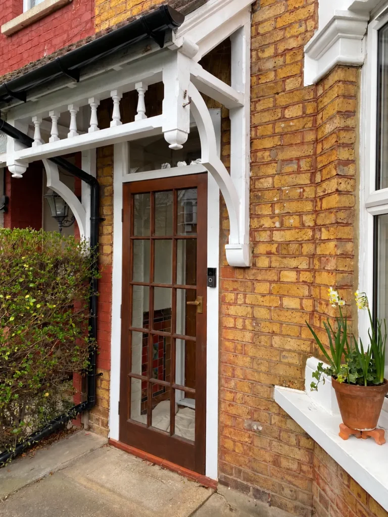 Front porch of a Victorian home in North London with white timber fretwork, turned spindles and a glazed timber outer door set in yellow stock brick