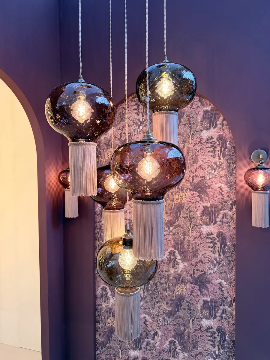 Cluster of Rothschild & Bickers hand-blown plum glass pendant lights with blush silk tassels against floral wallpaper at Decorex 2026
