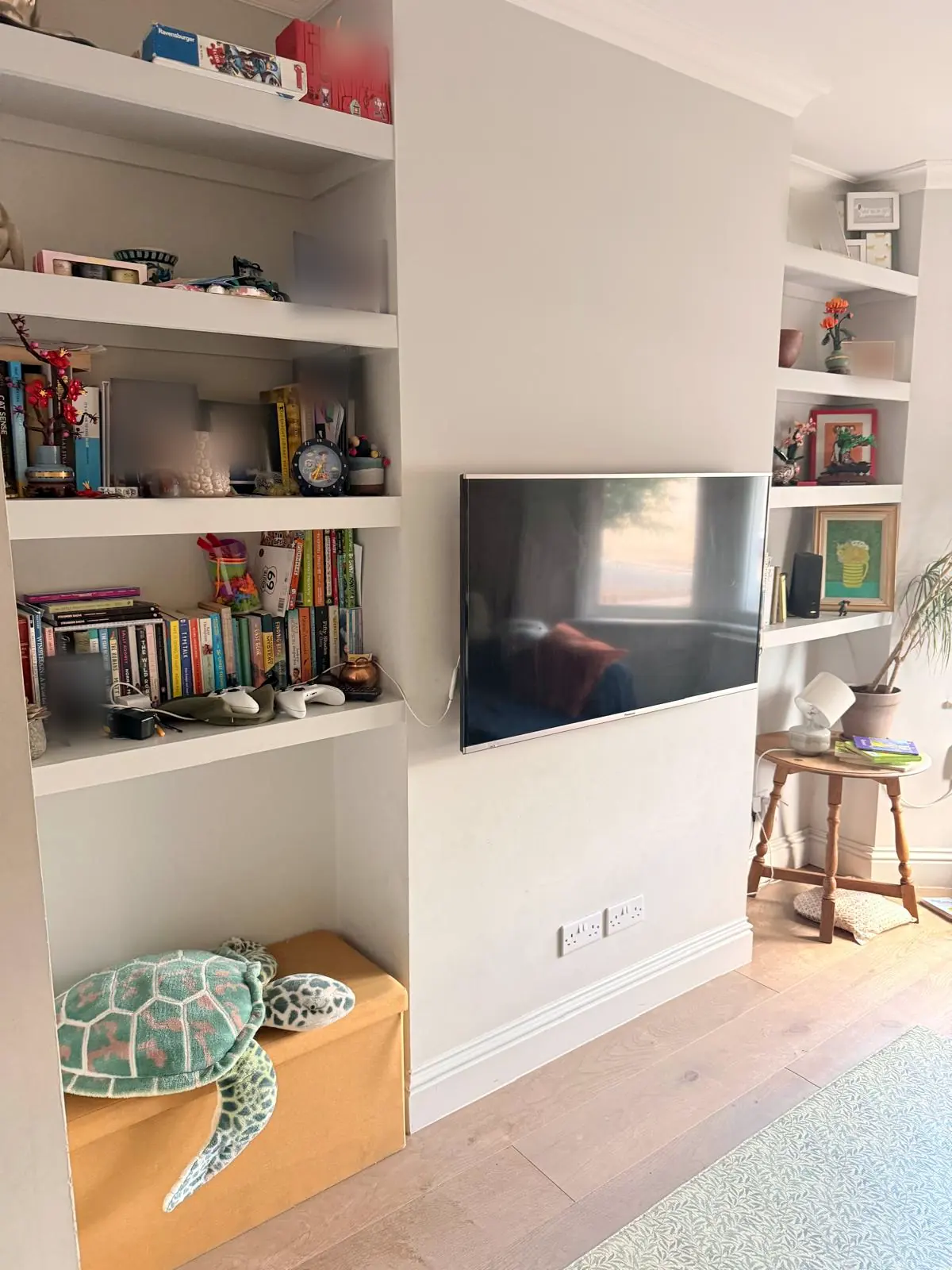 Before: the other side of the same front room, with painted alcove shelves either side of the chimney breast, a wall-mounted TV, a round wooden side table and an oak floor