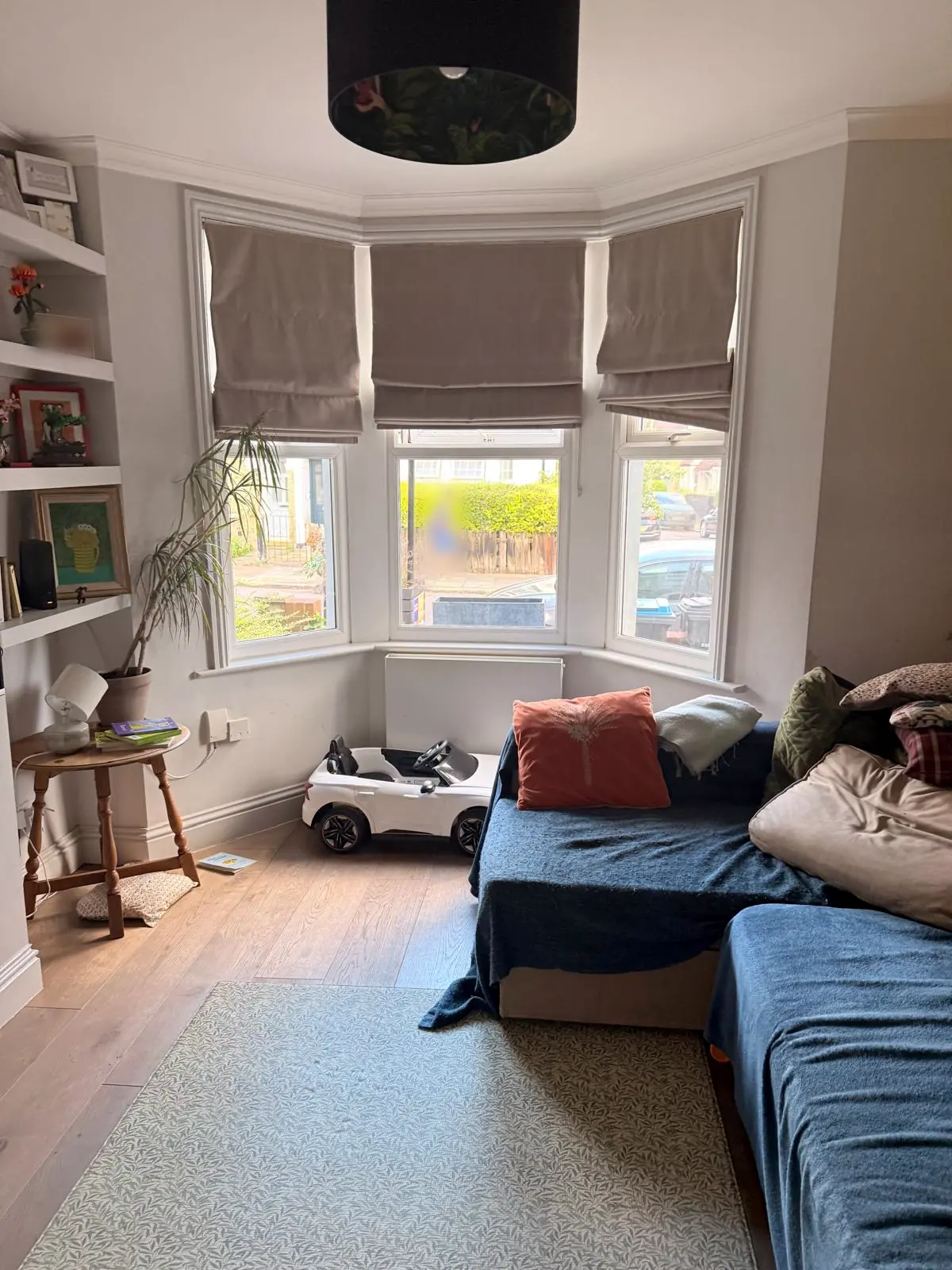 Before: the front room of a North London Victorian terrace, with grey walls, Roman blinds in the bay window, oak flooring and an existing sofa covered with blue throws